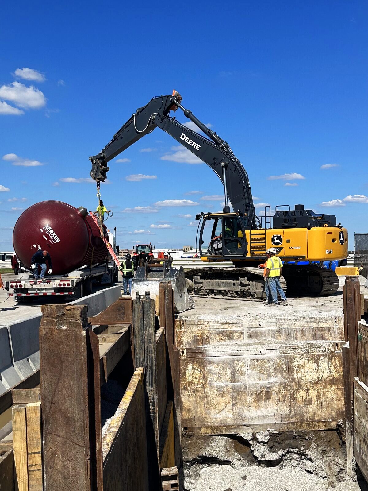 Excavator positioning an underground storage tank at a shored excavation during removal